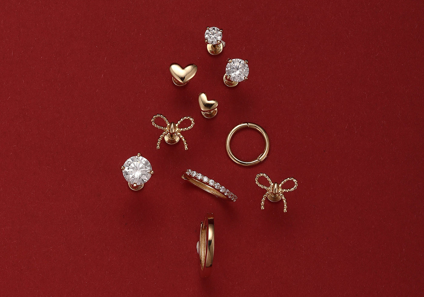 An assortment of classic gold hypoallergenic earrings, including studs and hoops, arranged in a Christmas tree shape on a festive red background.