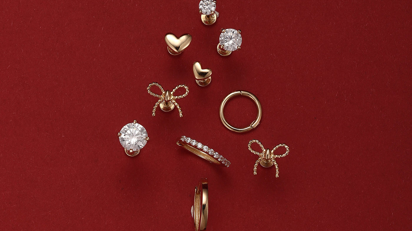 An assortment of classic gold hypoallergenic earrings, including studs and hoops, arranged in a Christmas tree shape on a festive red background.
