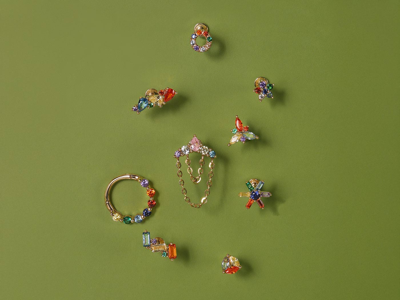 Colorful gemstone ear piercing studs and hoops in 14K gold for curated ear styling on green background