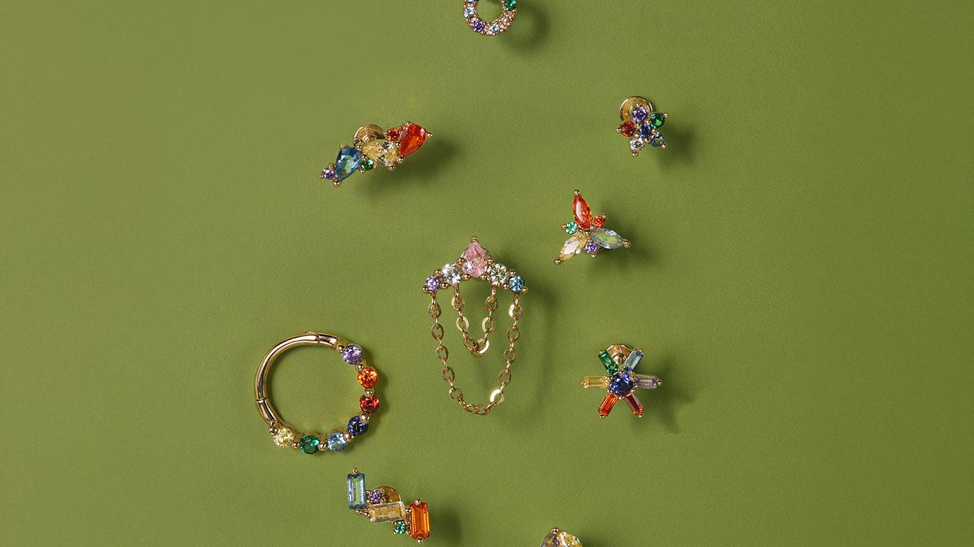 Colorful gemstone ear piercing studs and hoops in 14K gold for curated ear styling on green background