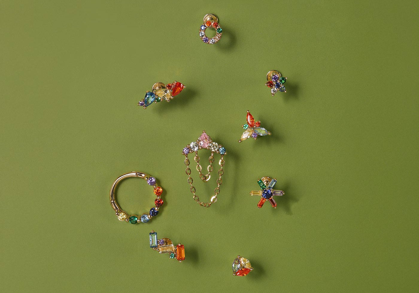 Colorful gemstone ear piercing studs and hoops in 14K gold for curated ear styling on green background
