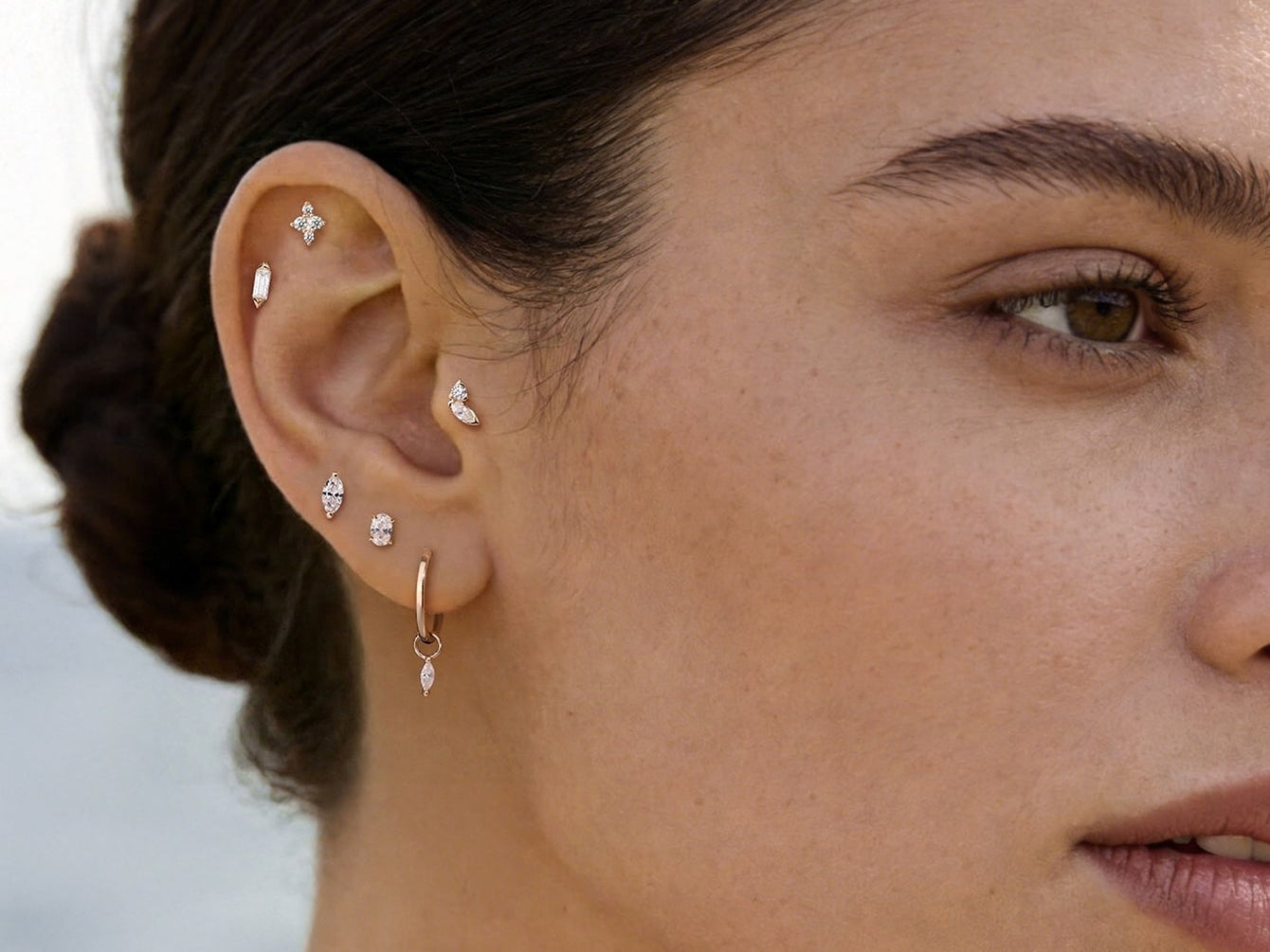 Gold earring stack featuring diamond flat studs, hoops, and marquise crystals across lobe and cartilage piercings.