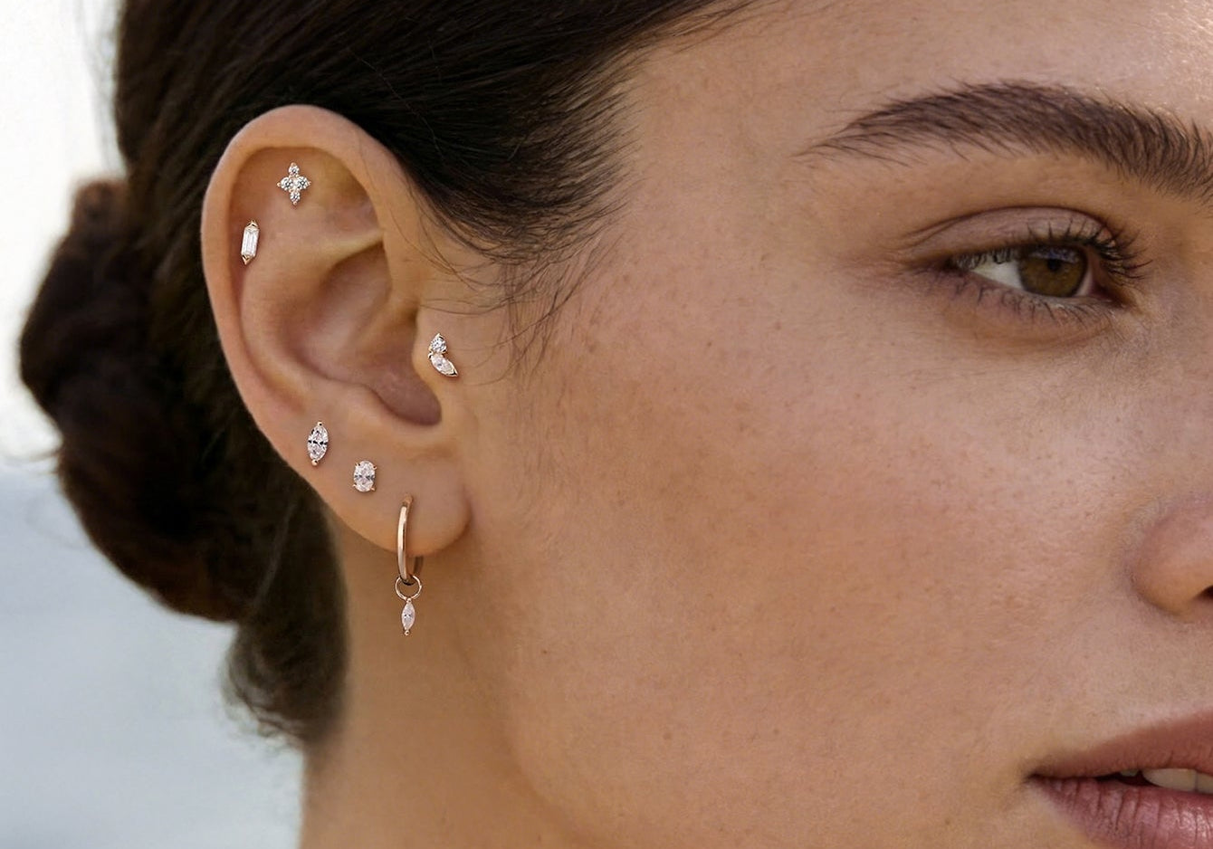 Gold earring stack featuring diamond flat studs, hoops, and marquise crystals across lobe and cartilage piercings.