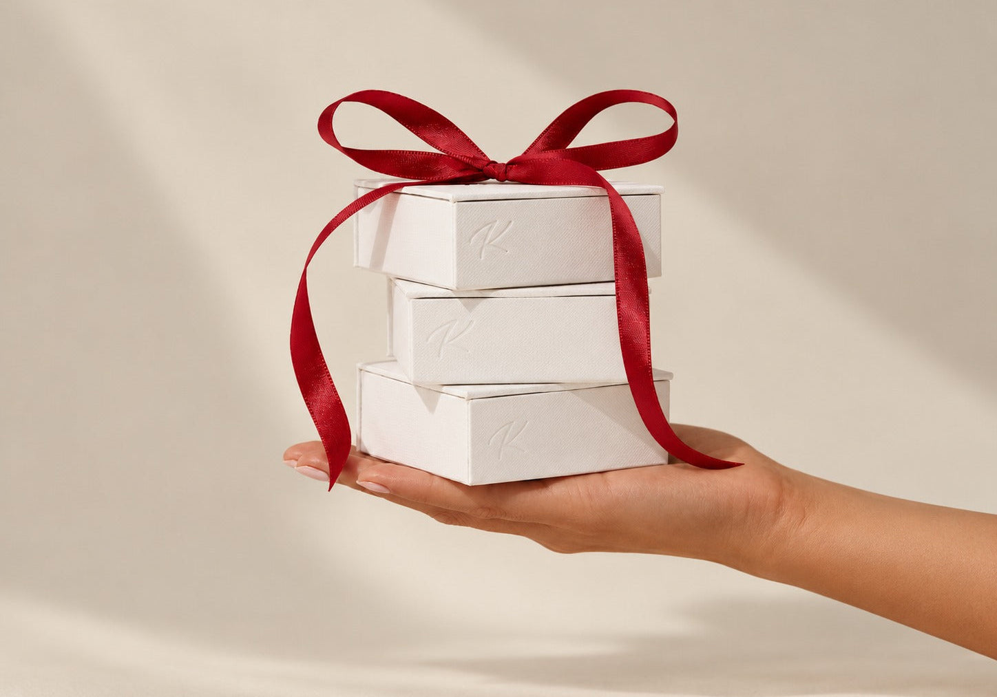 Three Kosiner Jewelry gift boxes tied with a red ribbon, held in a hand