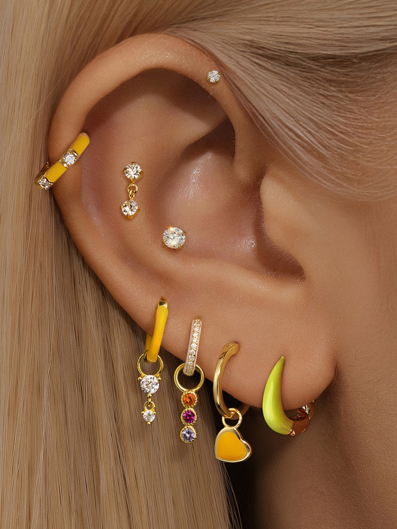 Multiple gold-plated sterling silver ear piercings with cubic zirconia, including solitaire studs and charms for styling.