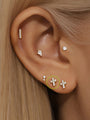 14K solid gold lucky cross ear piercing stud with clear cubic zirconia on human ear, styled with multiple earrings.