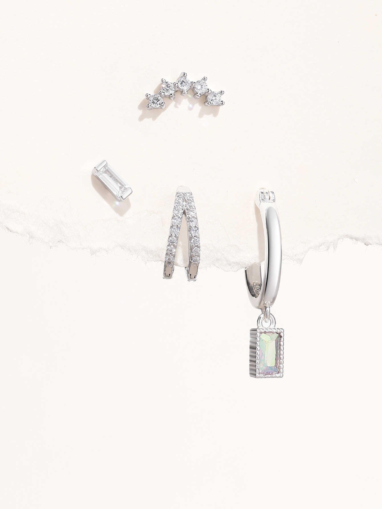 Collection of 925 sterling silver earrings with cubic zirconia: curved stud, baguette stud, pavé hoops, and drop earring.
