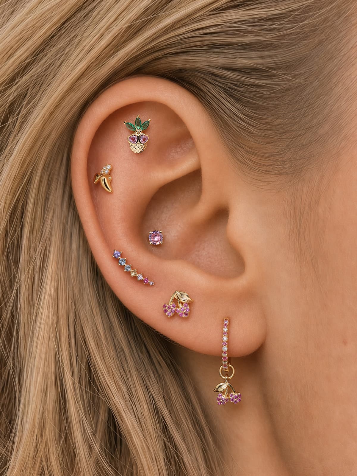 Layered full ear stack styling of KOSINER Orchard whimsical fruit collection, pink cherry flat back stud matched with pineapple, banana, rainbow gradient, solitaire gem cartilage piercings