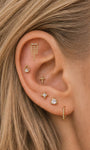 Soft curated multi-piercing ear stack featuring KOSINER Perléa triple chain tassel flat back stud placed on upper helix, styled with teardrop outline stud, beaded cross rook stud, four-point star lobe stud, heart CZ stud and plain beaded huggie hoop, elegant layered everyday ear piercing design
