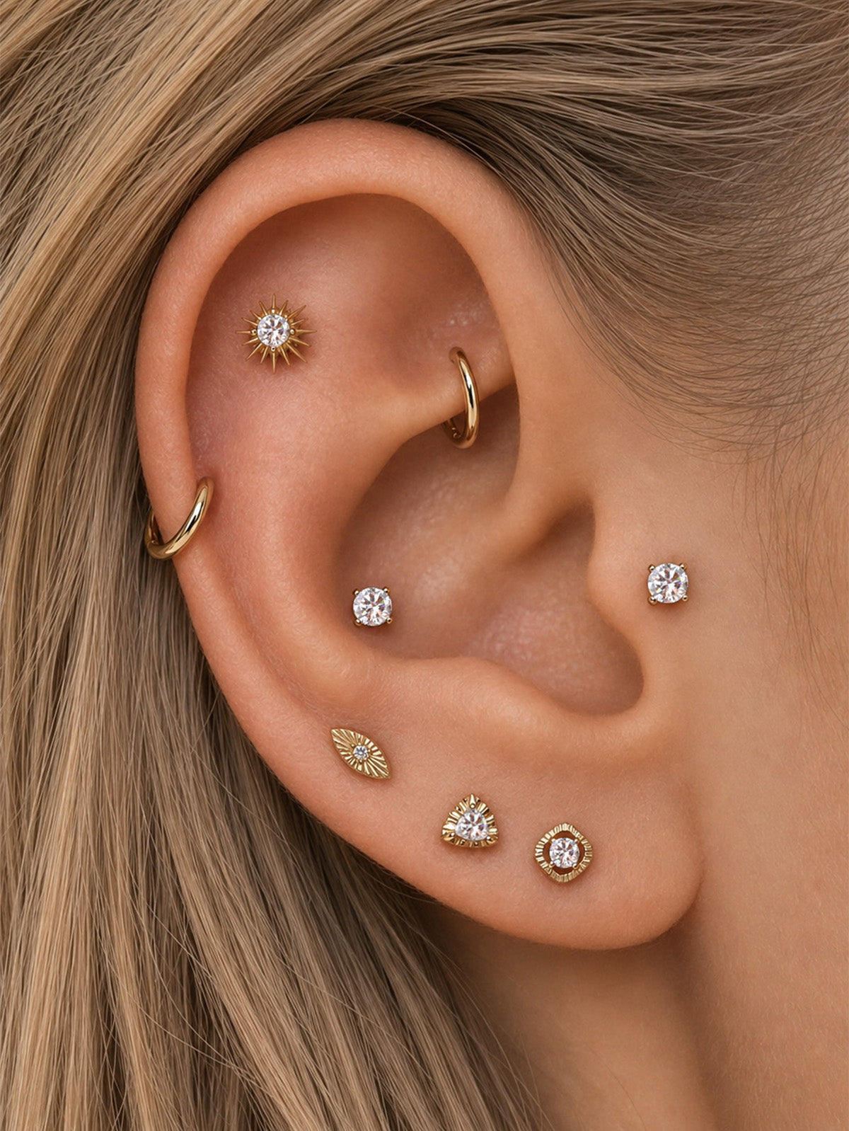 Refined curated ear styling featuring KOSINER Étoile marquise textured flat back stud on earlobe, matched with sunburst, triangular, square gem studs and gold hoop rings, minimalist luxe multi-piercing daily ear layout