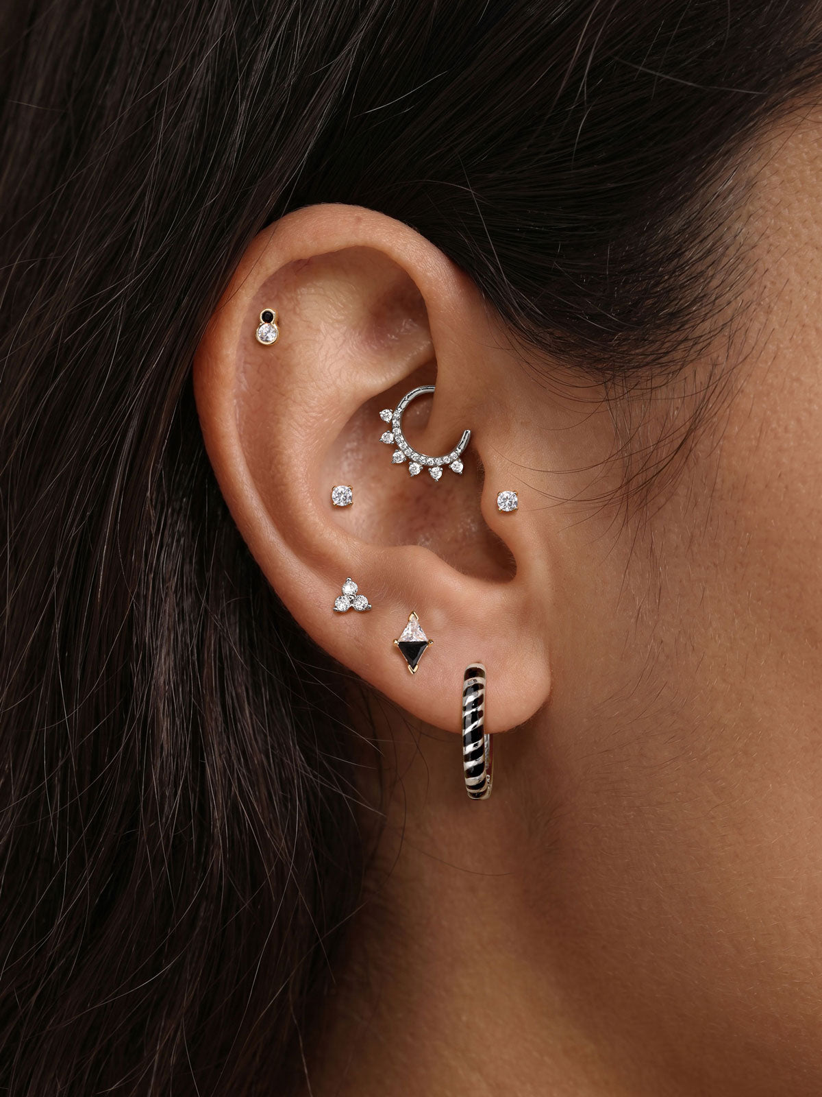 Edgy personalized full ear stacking styling with KOSINER Puzzle zebra stripe sterling silver hoop earring, paired cz cartilage studs, triangular two-tone studs, pave crescent daith hoop, bold animal pattern modern multi-piercing ear look