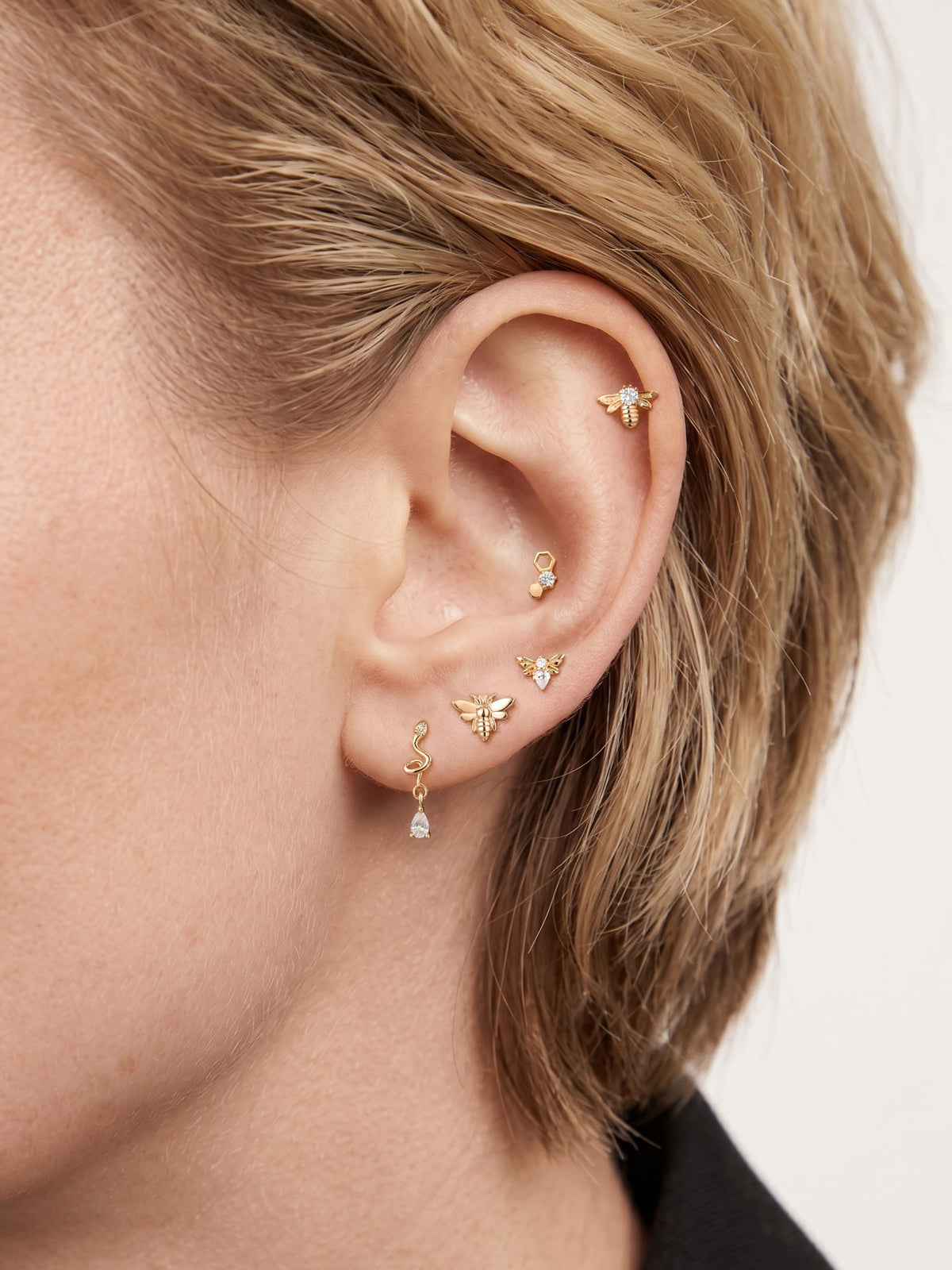 Model wearing 14K solid gold honeycomb flat back stud on inner helix, curated layered ear stack with assorted gold cartilage piercings, blonde hair ear styling lifestyle photo