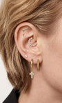 Trendy layered full ear stack styling with KOSINER gold cross drop hoop earring, paired sunburst cz rook hoop, chain dangle helix stud, baguette flat studs, textured bead hoop, minimalist edgy cartilage ear piercing stacking aesthetic