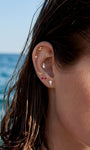 Coastal summer ear stacking styling with KOSINER Seaspritz 14K gold wine glass flat back stud, matched bikini, starfish and other vacation series piercing studs, layered multi-piercing look against bright ocean scenery