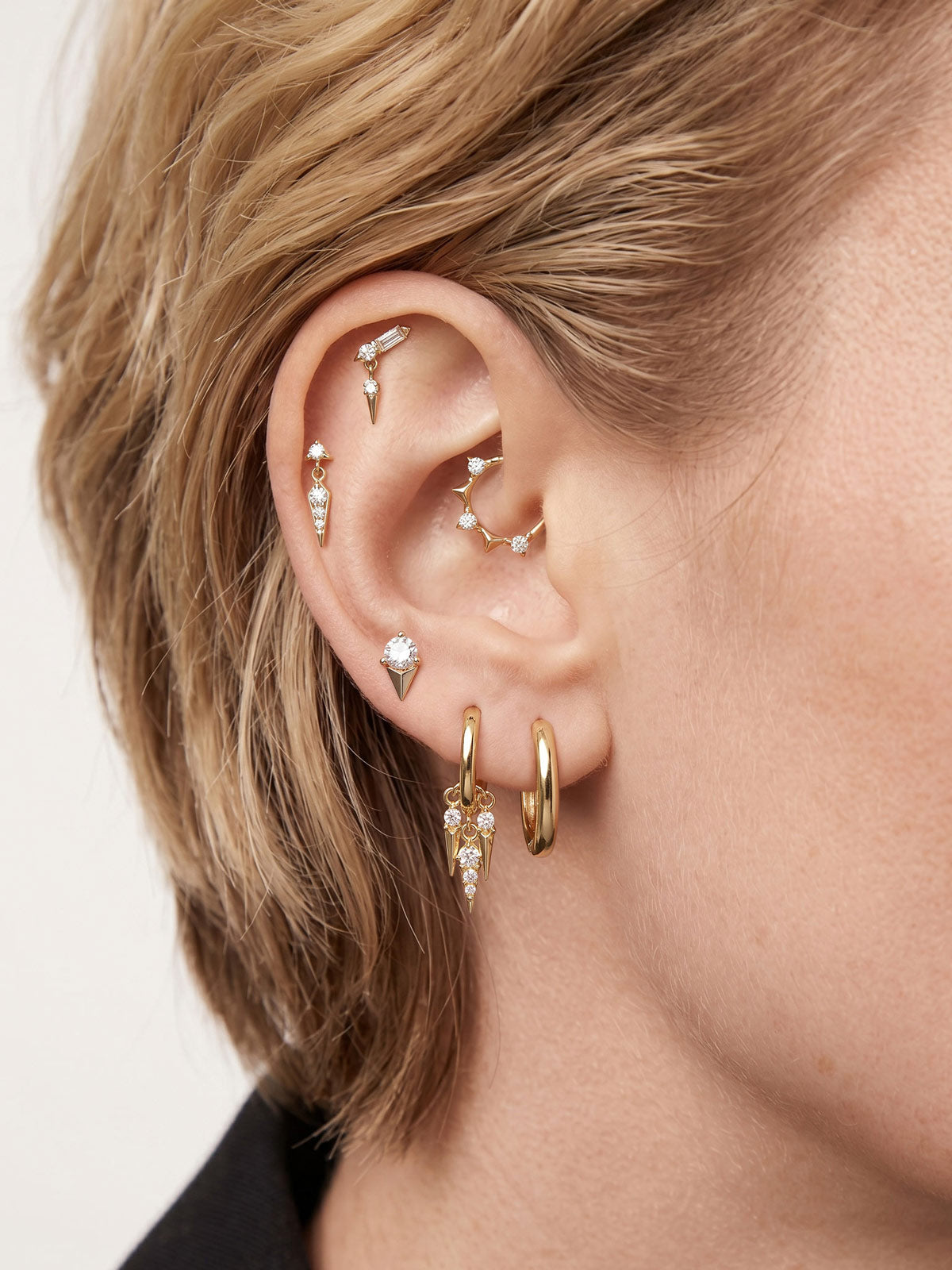 Edgy layered full ear stacking aesthetic with KOSINER Prism three-spike geometric daith clicker hoop, paired spike dangle flat back studs, baguette helix piercing, triple spike drop lobe hoop, modern sharp-line personalized multi-position ear piercing styling