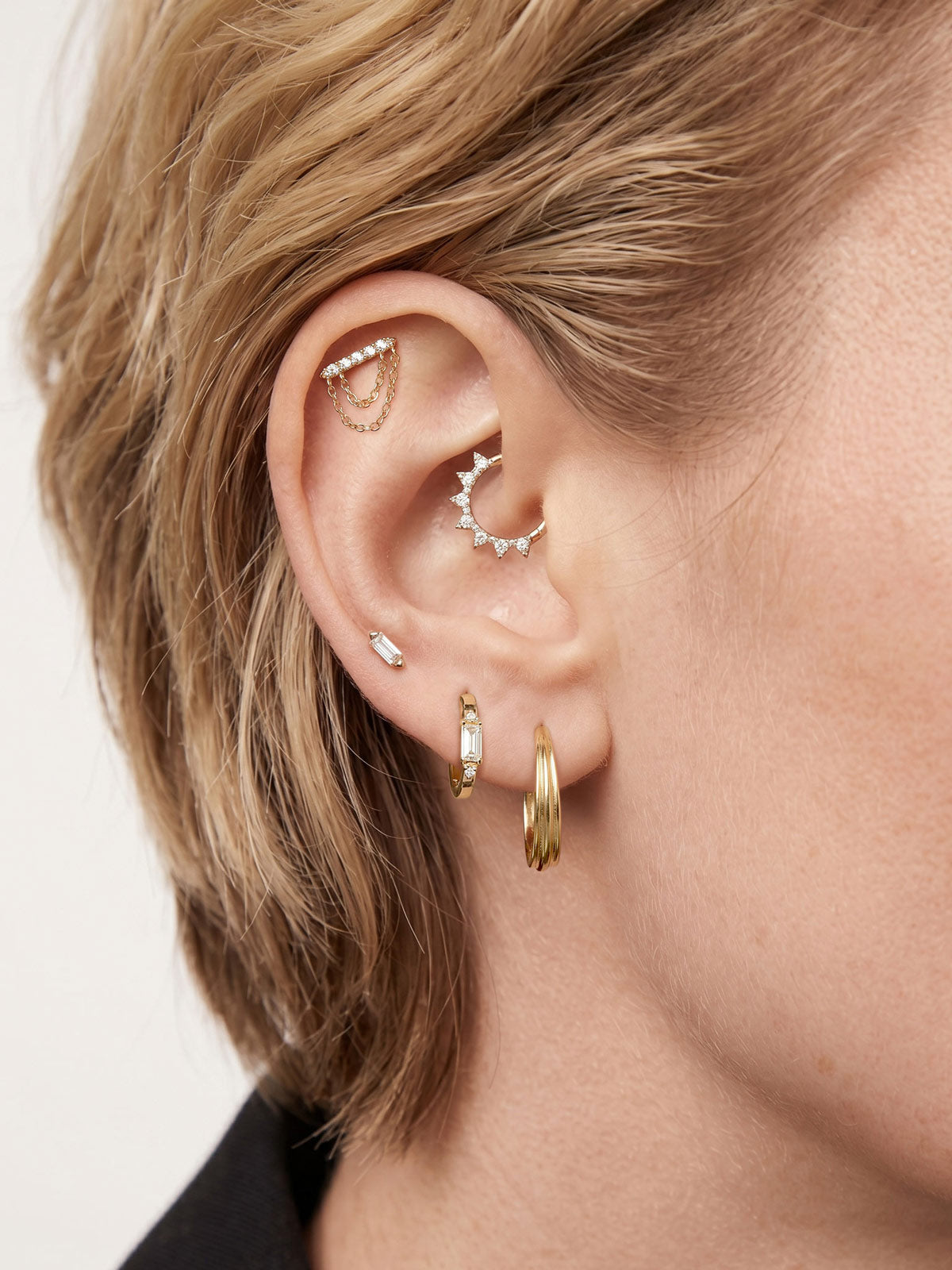 Layered full ear stack styling with KOSINER Prism baguette clicker hoop, paired sunburst cz rook hoop, chain drop helix stud, tiny baguette flat stud, triple gold hoop lobe piercing, trendy minimalist cartilage ear stacking aesthetic