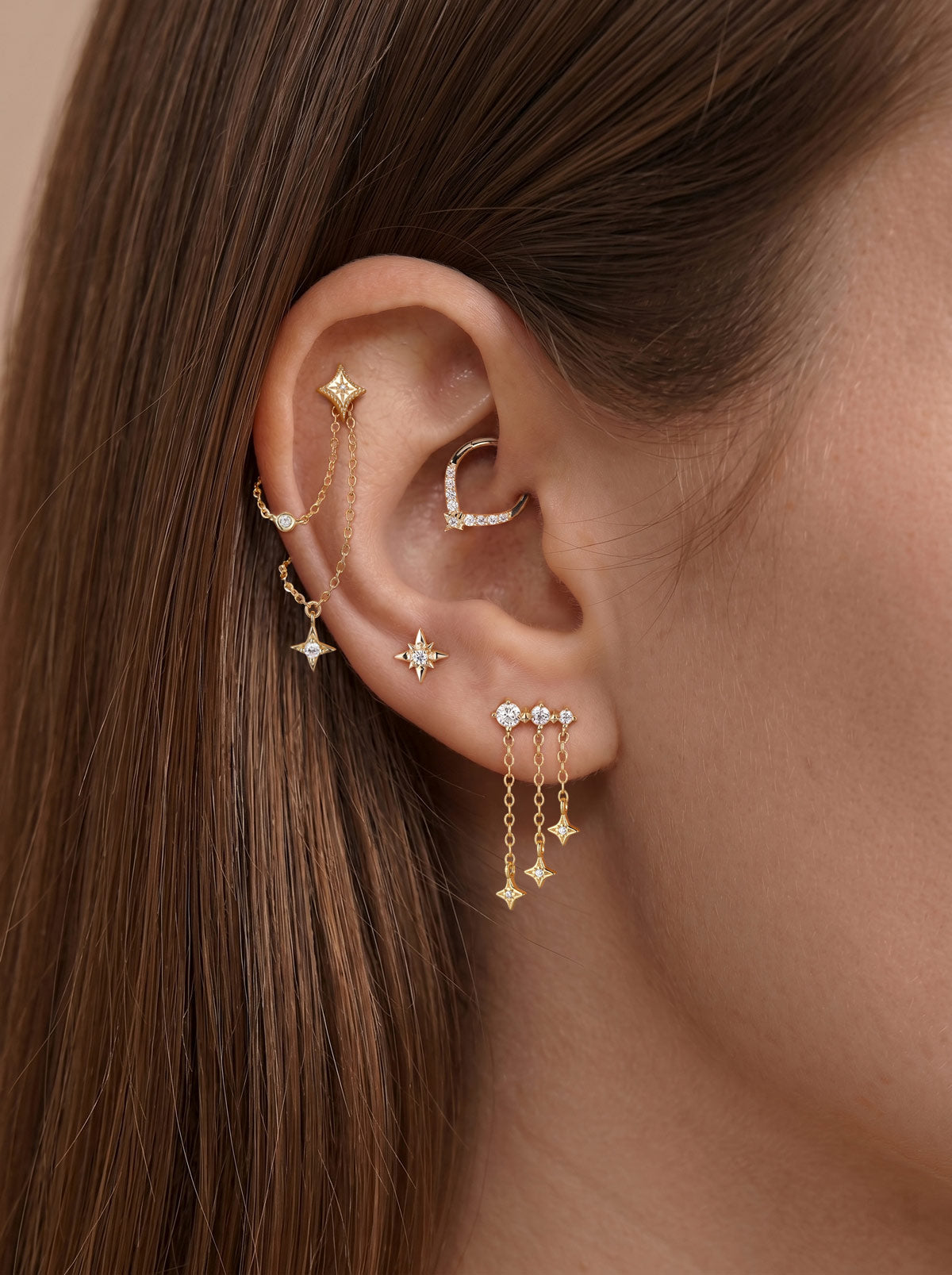 Elegant curated multi-piercing ear stack featuring KOSINER Starlight delicate four-point star flat back stud fitted on upper helix, styled with matching star motif accessories, marquise stone daith hoop, dual inter-piercing chain, teardrop outline stud and dangling star drop earrings, sophisticated layered ear styling design