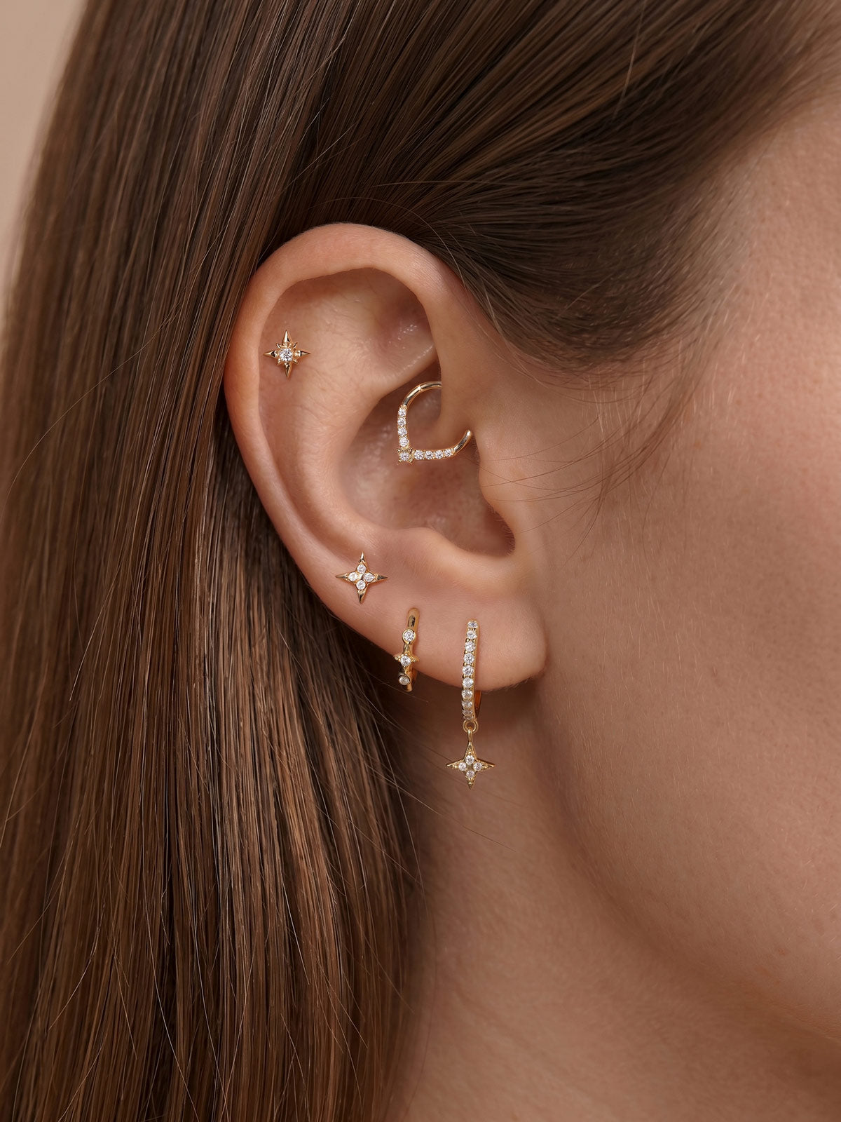 Elegant curated multi-piercing ear styling featuring KOSINER Starlight four-point star teardrop daith clicker hoop fitted in daith piercing, paired with matching north star helix stud, four-point star mid-helix stud, mini star drop lobe hoop, and vertical star detail stud for cohesive star themed ear stack