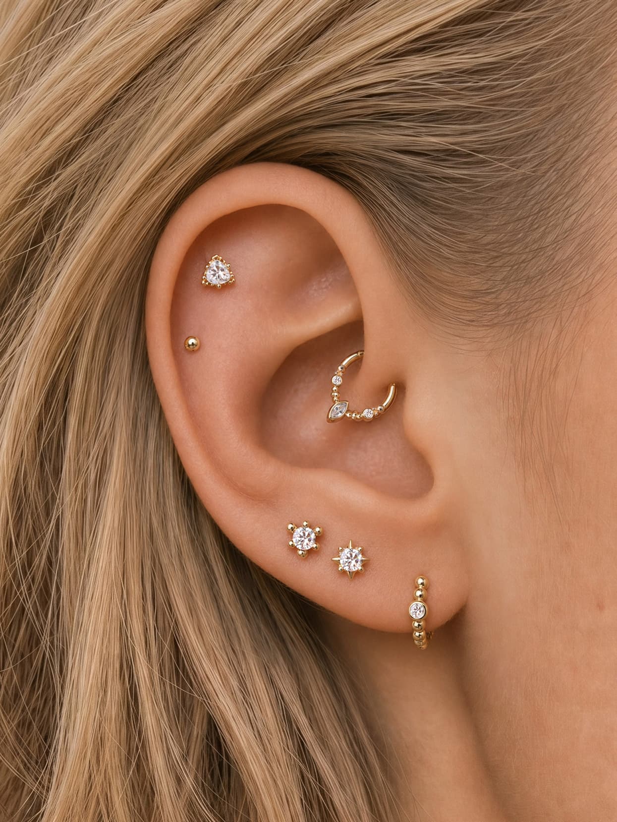 Soft minimalist curated multi-piercing ear stack featuring KOSINER Perléa beaded hoop on earlobe, styled with star-shaped crystal studs, tiny ball stud and decorative helix hoop, elegant everyday layered ear piercing design