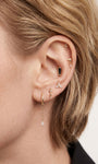 Blonde model curated ear stack styled with 14K gold kite drop charm attached on lobe hoop, layered goth piercing jewelry closeup lifestyle photo
