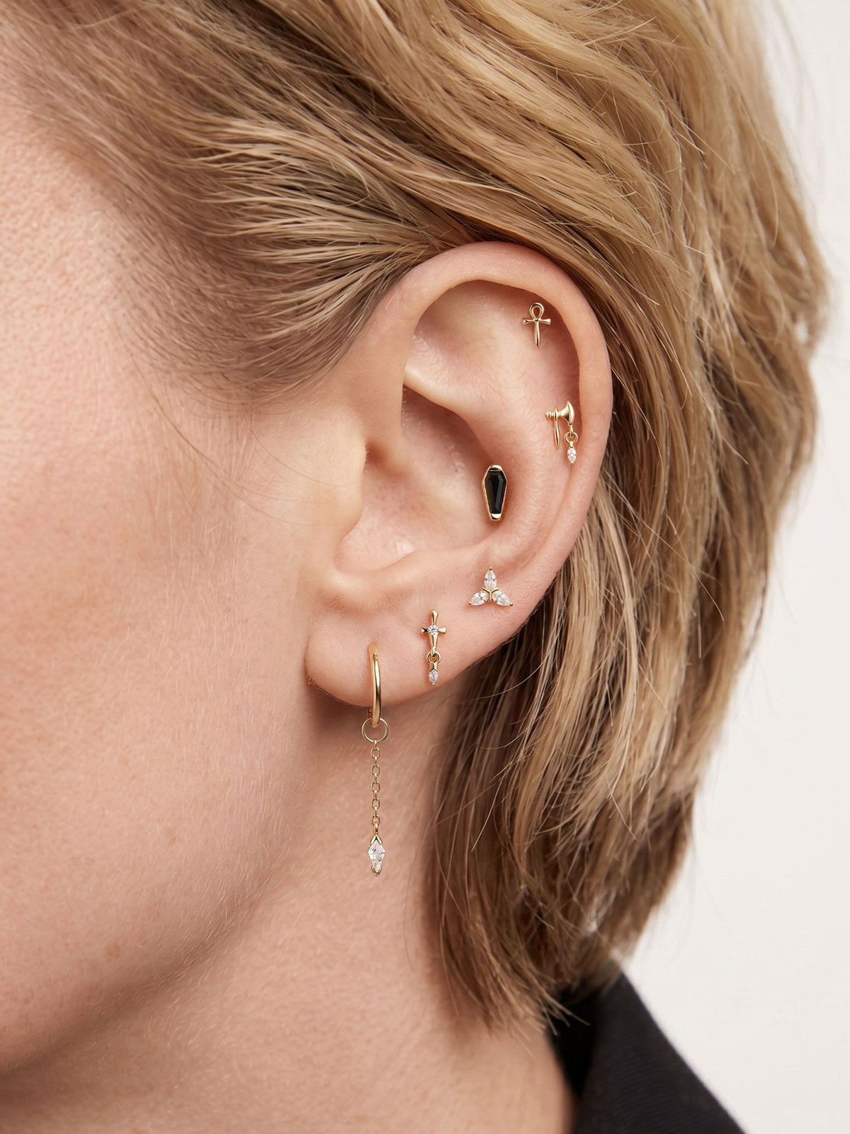 Blonde model curated ear stack styled with 14K gold kite drop charm attached on lobe hoop, layered goth piercing jewelry closeup lifestyle photo
