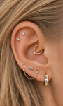 Sophisticated curated multi-piercing ear stack featuring KOSINER Perléa blue marquise eye flat back stud, paired with north star helix studs, marquise detail daith clicker, dual chain linked lobe piercing, teardrop outline stud and two-tone huggie hoop, elegant layered ear styling design