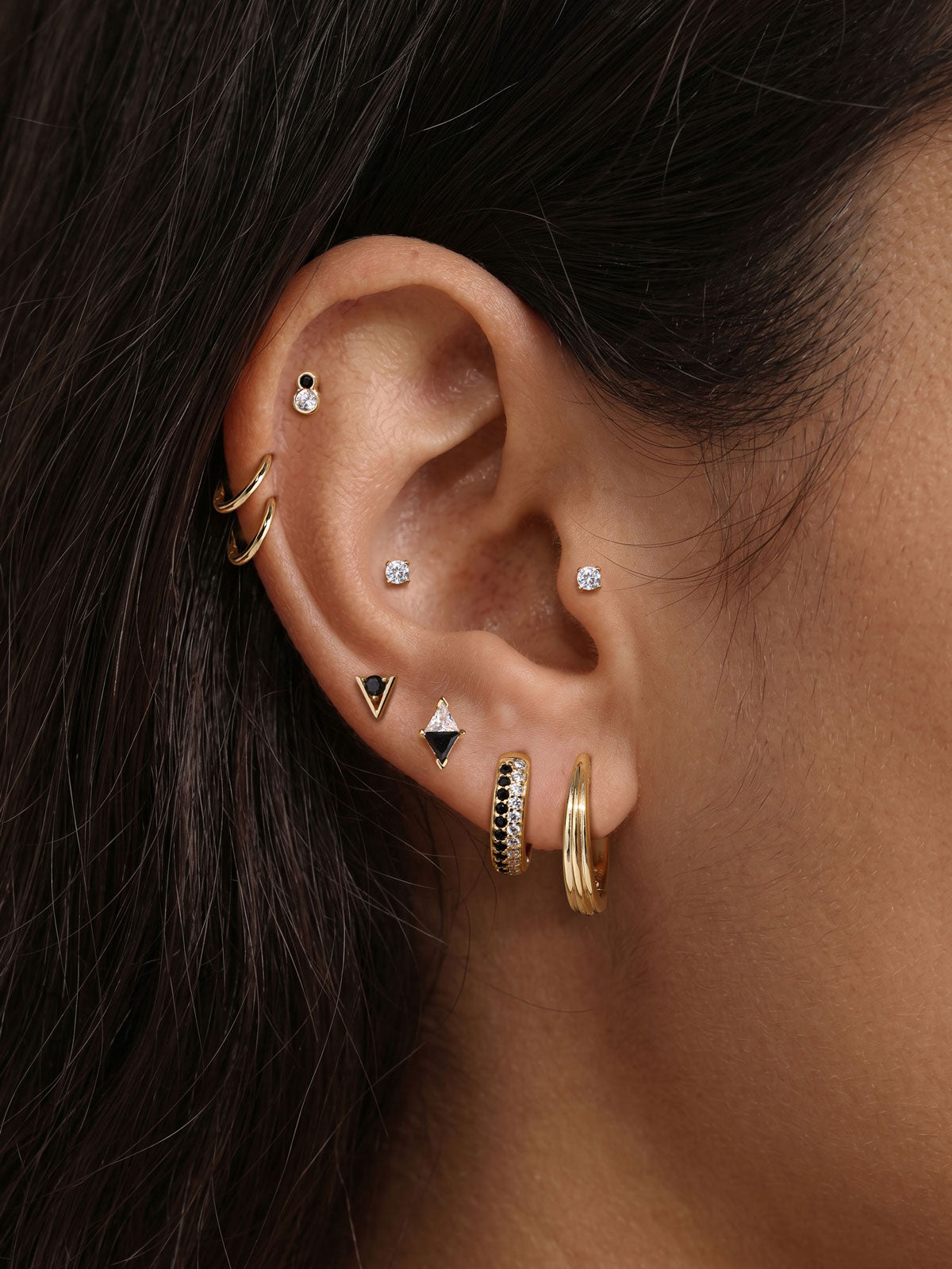 Stylish layered full ear stacking aesthetic with KOSINER Puzzle two-tone bezel figure 8 flat back helix stud, paired triangular two-tone studs, two-tone pave hoop, tiny plain cz cartilage studs, contemporary contrast design multi-piercing ear styling