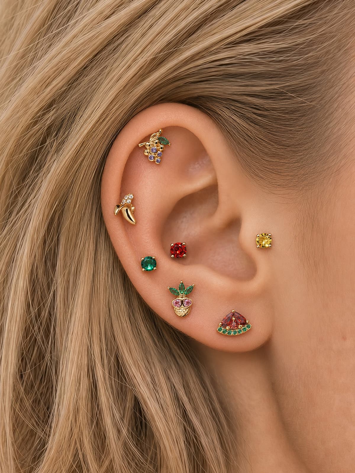 Layered full ear stack styling of KOSINER Orchard fruit jewelry line, purple grape flat stud matched with banana, pineapple, watermelon, round solitaire gem cartilage piercings