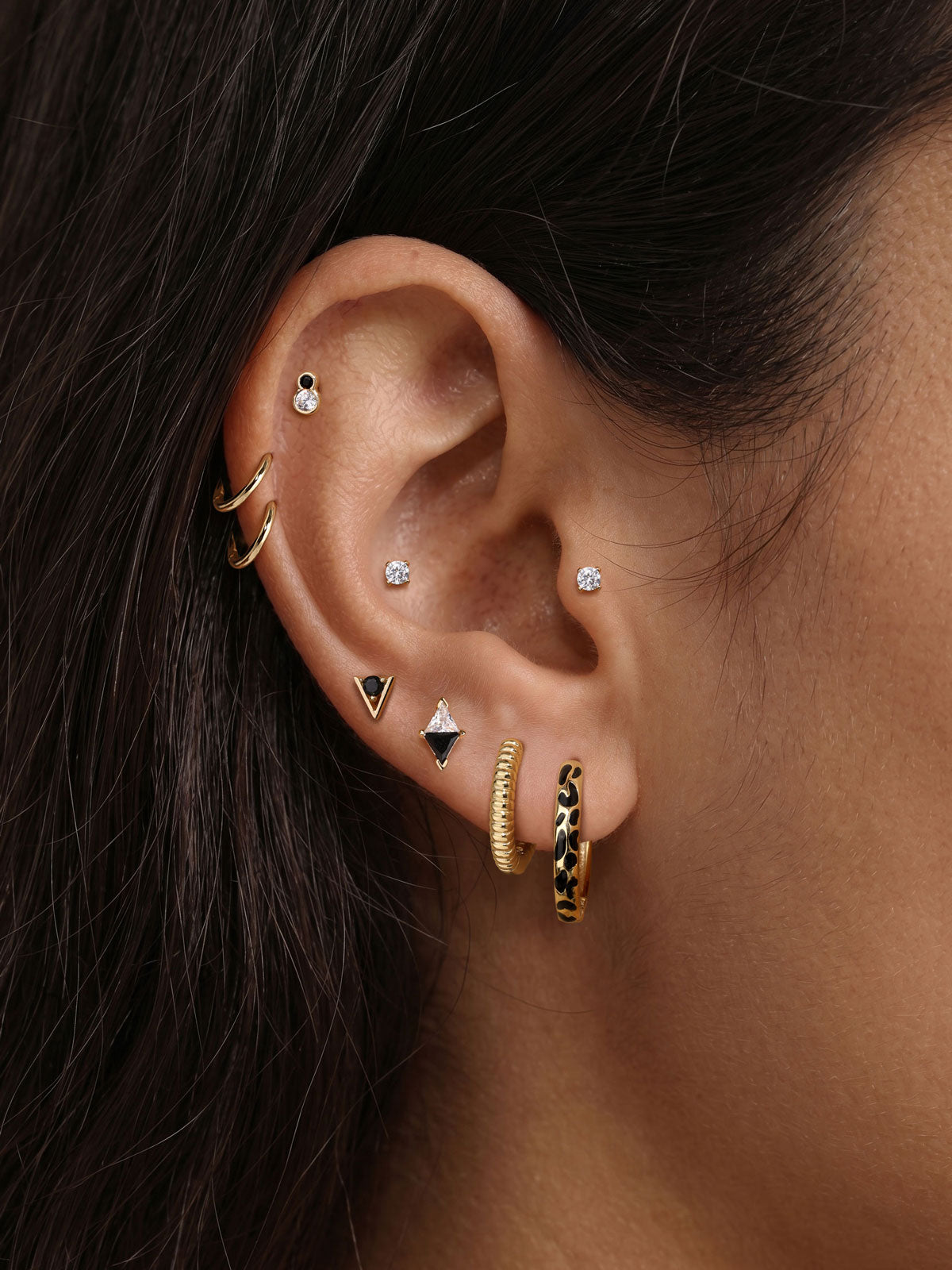 Trendy multi-piercing ear stacking look with KOSINER Puzzle black enamel leopard print sterling silver hoop earring, matched tiny cz studs, geometric triangle studs, textured gold hoops, chic edgy everyday ear styling