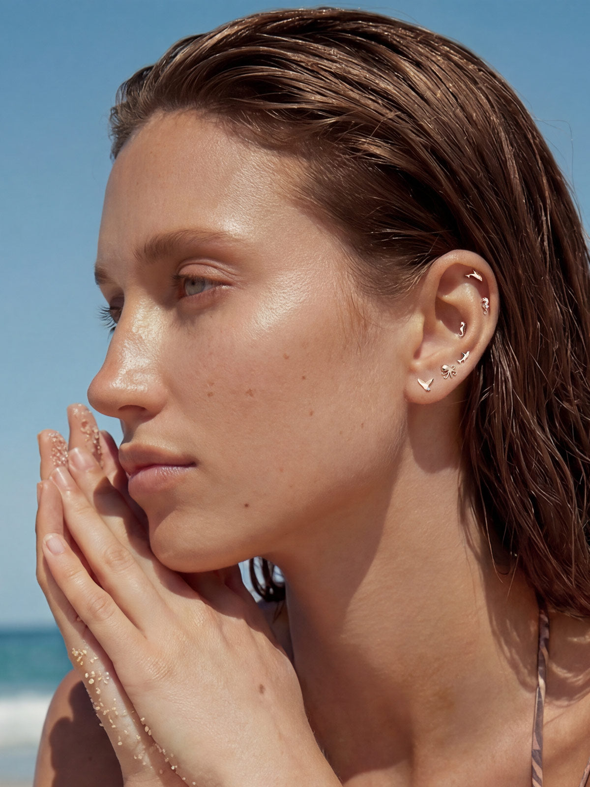 Coastal-themed full ear stacking look with KOSINER 14K gold whale flat back helix stud, matched seahorse, shark, octopus, mermaid tail ocean animal piercing studs, seaside vacation aesthetic multi-piercing ear styling by the sea