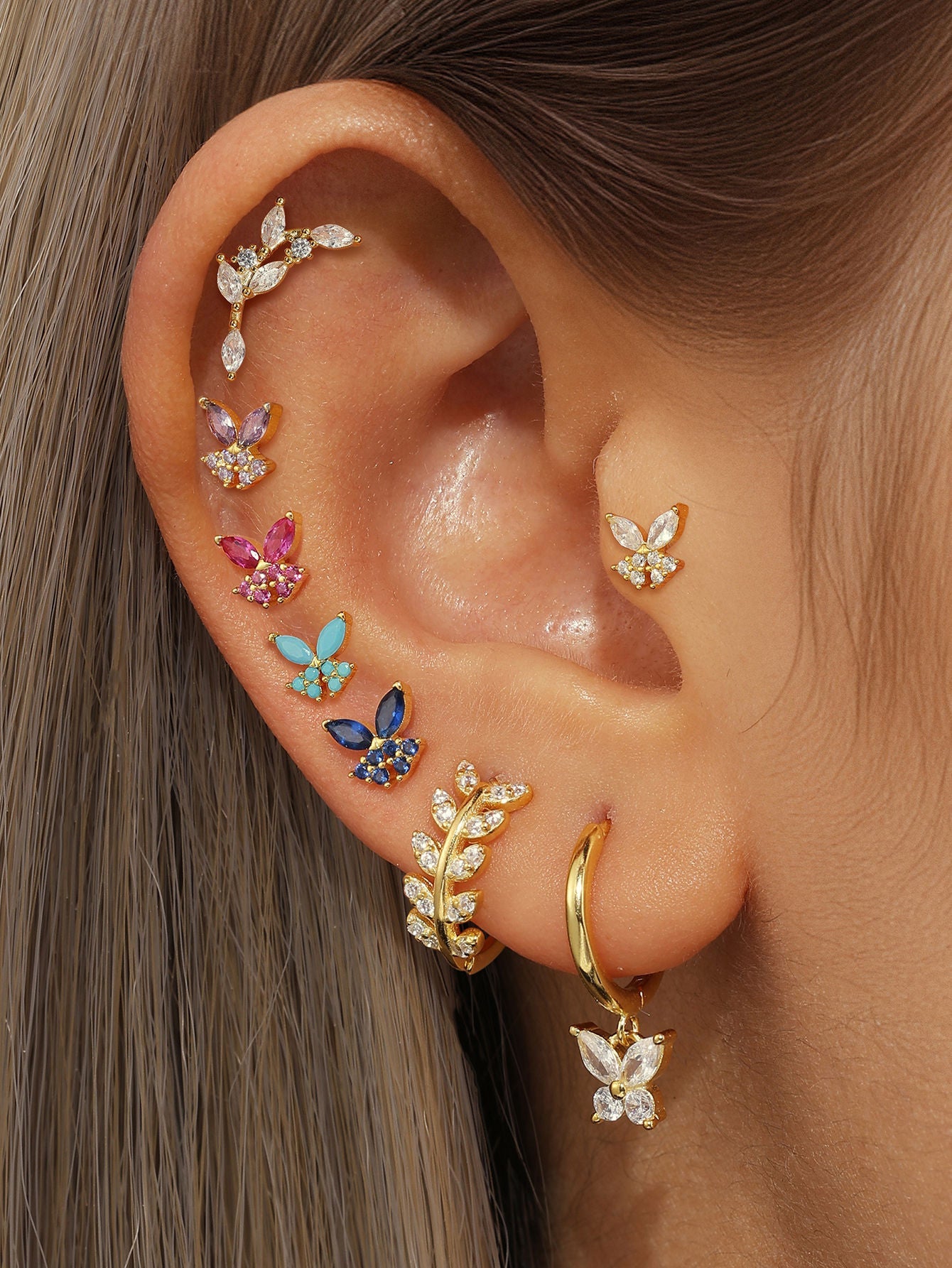 Collection of 925 sterling silver ear piercing studs: gold-plated butterfly and silver leaf with cubic zirconia, on ear.