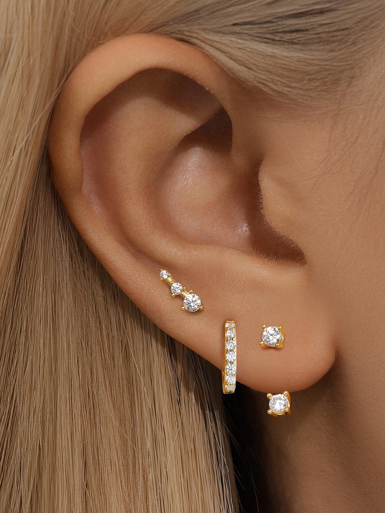 3-piece 18k gold-plated cubic zirconia earring set: hoop, ascending stud, square stud on a woman's ear.