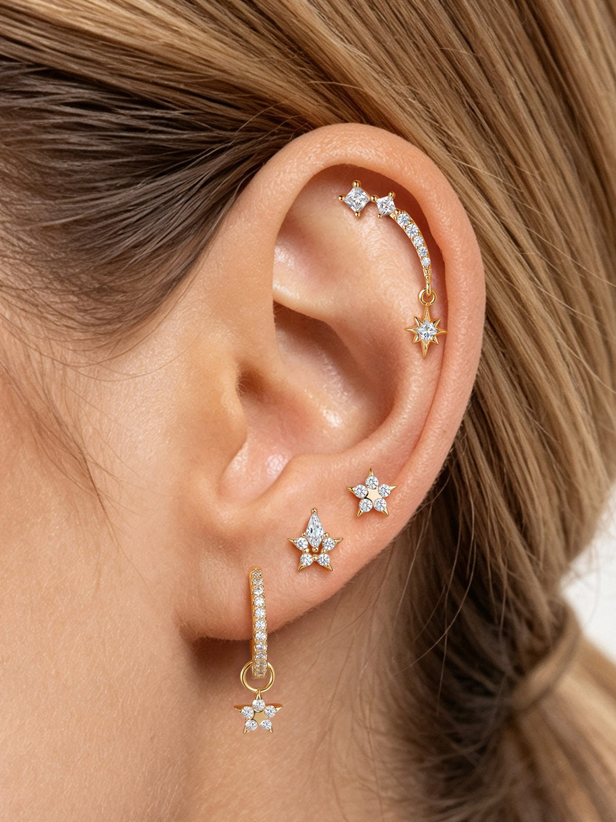 Angled view of KOSINER Rising Star gold-plated dangle hoop with clear stones and a five-pointed star charm
