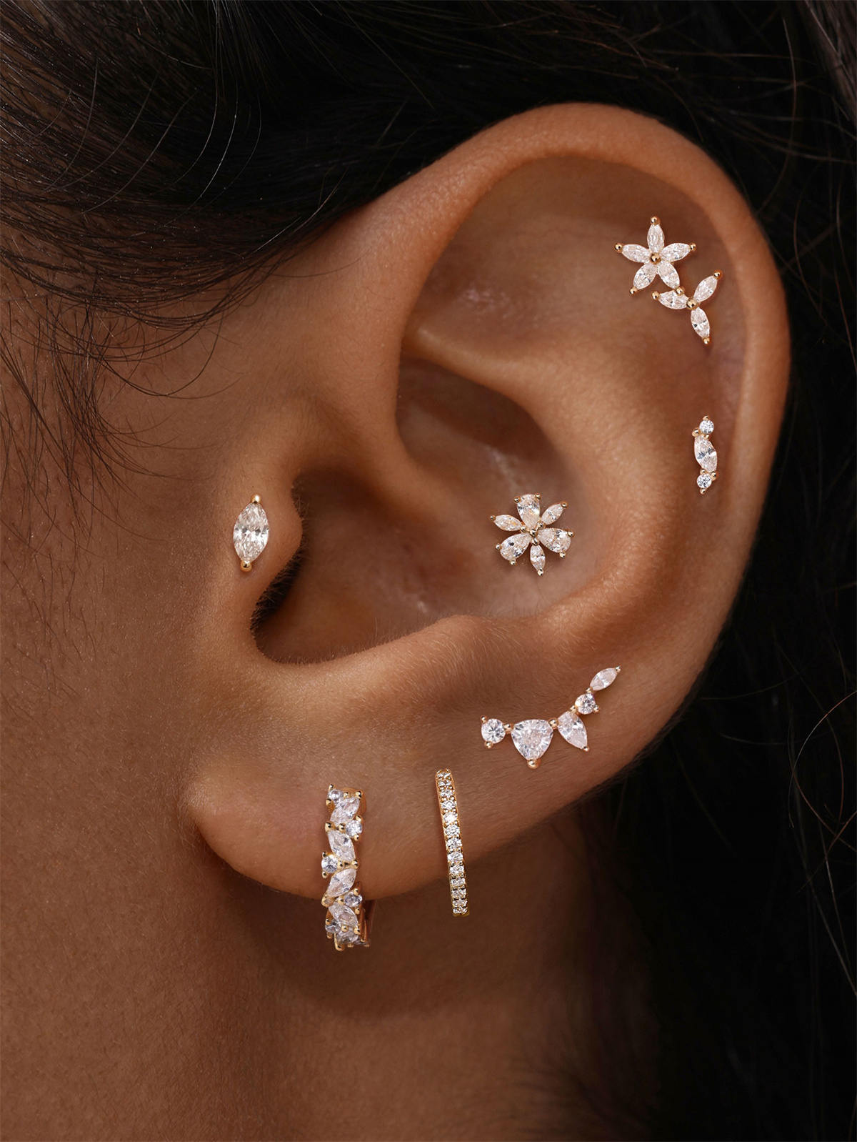 Close-up of ear stacked with dainty KOSINER marquise petal flower cz flat back studs and hoops, elegant multi-ear piercing aesthetic