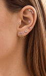 Soft feminine ear stack featuring KOSINER Pink Ritual triple-chain pendant piercing stud, coordinated with wing, heart lock and round gem piercings, natural close-up of wearable cartilage matching design