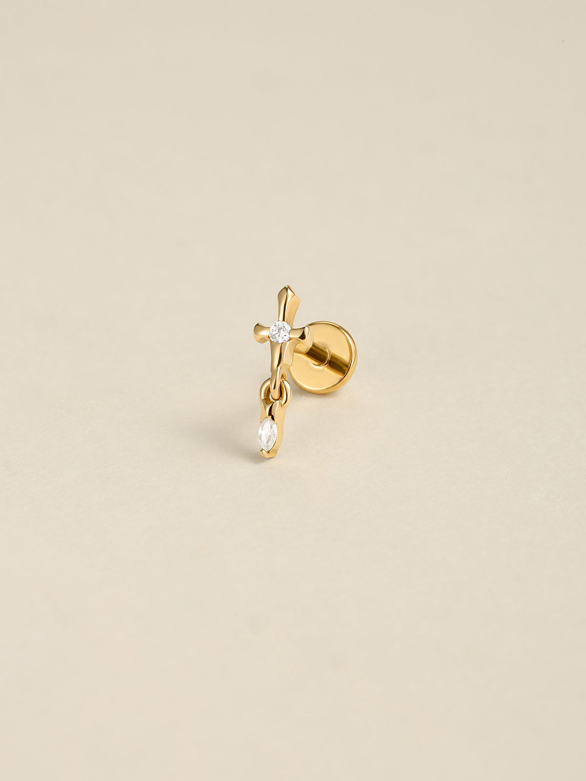 Angled still life shot of 14K solid gold broken sword drop flat back labret stud, clear CZ dangle piercing jewelry on soft beige background