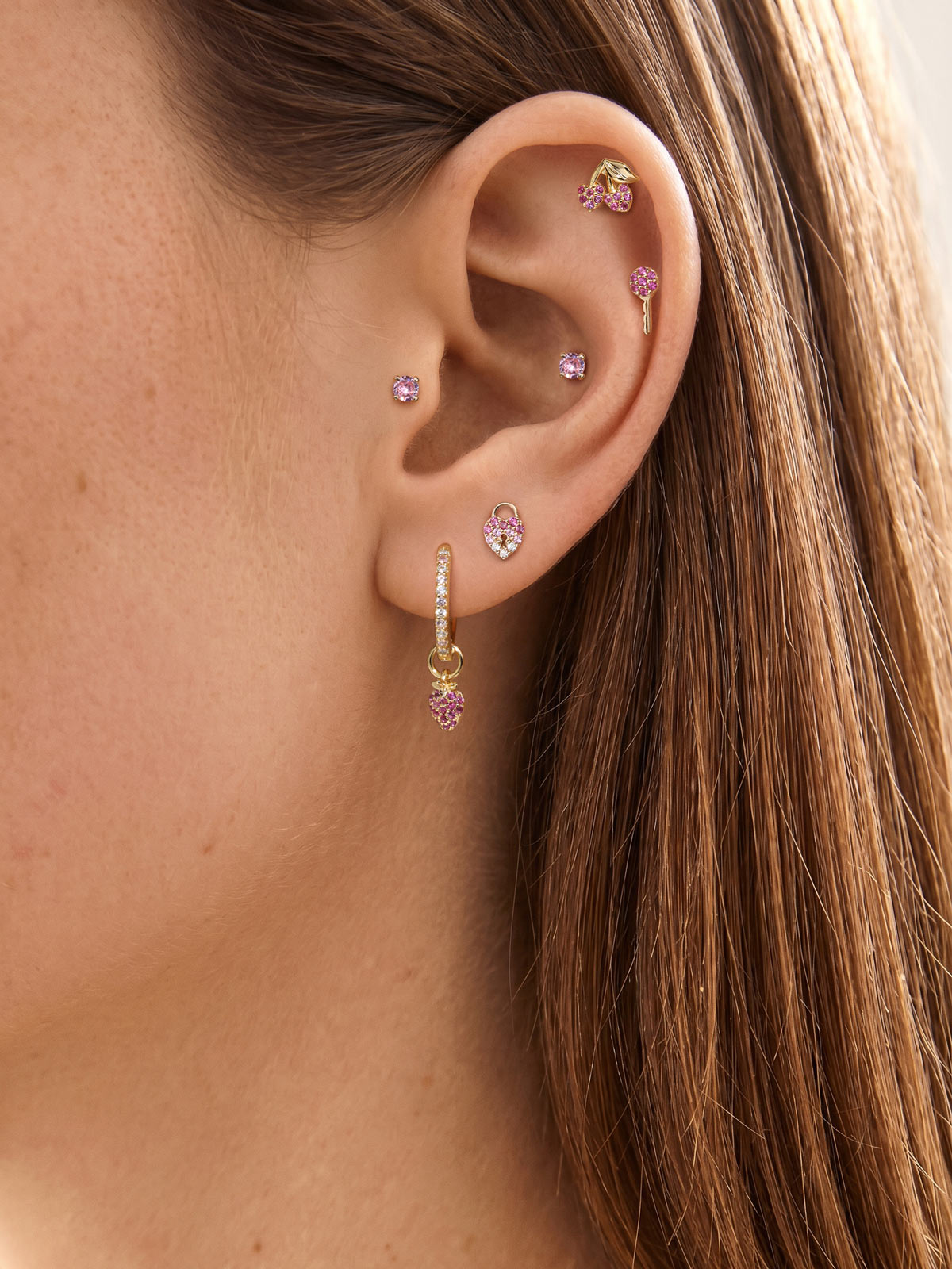 Soft feminine ear stack featuring KOSINER Pink Ritual heart lock piercing stud, coordinated with hoop pendant, cherry and tiny round studs, natural close-up of versatile ear matching design