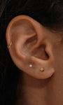 Close-up ear shot with KOSINER Étoile sunburst CZ flat back stud worn on earlobe, matched with simple solitaire stud and thin gold hoop, minimalist dainty everyday piercing combination