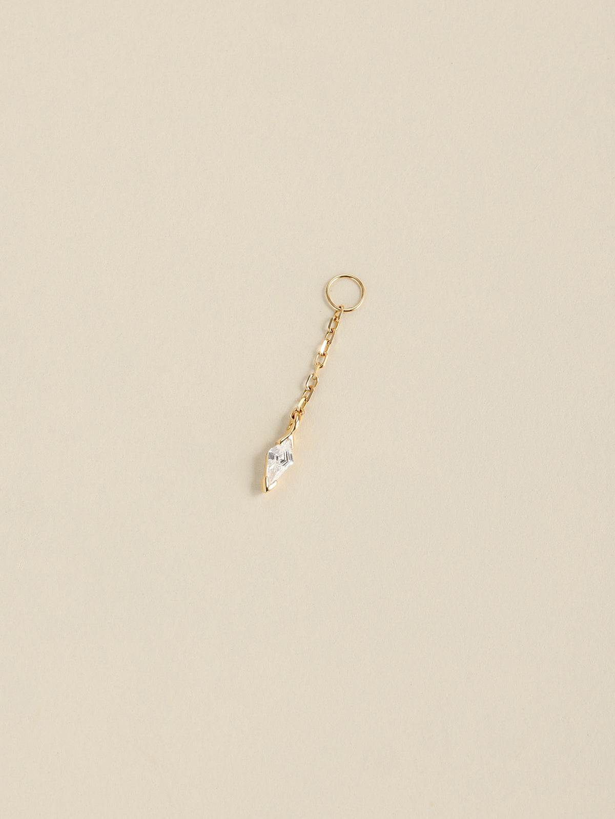 Angled still life shot of 14K solid gold kite drop chain charm, faceted kite CZ pendant on soft neutral beige background