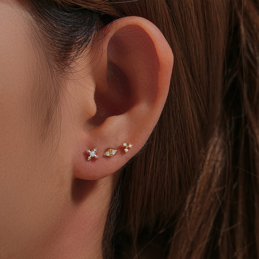 Three petite sterling silver & gold-plated CZ ear studs: starburst, eye, floral. Shown on earlobe.