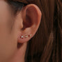 Three petite sterling silver & gold-plated CZ ear studs: starburst, eye, floral. Shown on earlobe.