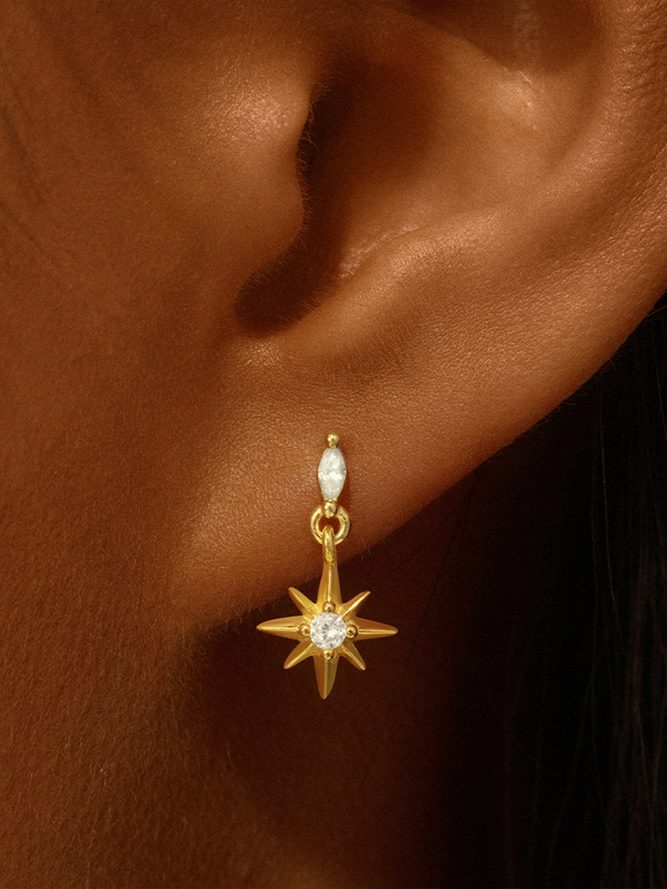 18kt gold plated 925 sterling silver stud earring with octagonal cubic zirconia and starburst charm worn on ear.