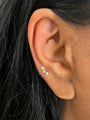 18kt gold plated sterling silver ear stud with three round cubic zirconia stones in a vertical line, worn on ear.