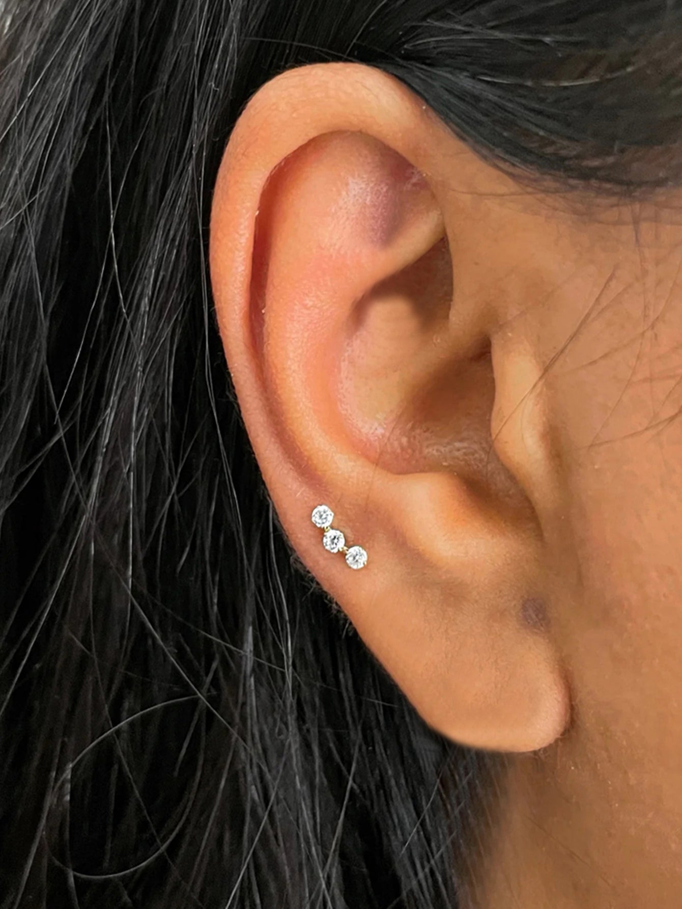18kt gold plated sterling silver ear stud with three round cubic zirconia stones in a vertical line, worn on ear.