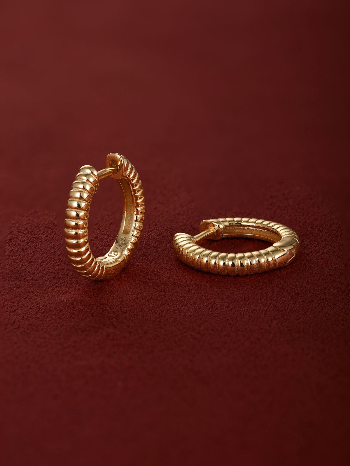 Pair of KOSINER Essentials 925 sterling silver gold-plated ridge textured clicker hoop earrings, ribbed corrugated surface detail, internal stamp marking, shot on soft burgundy suede fabric background