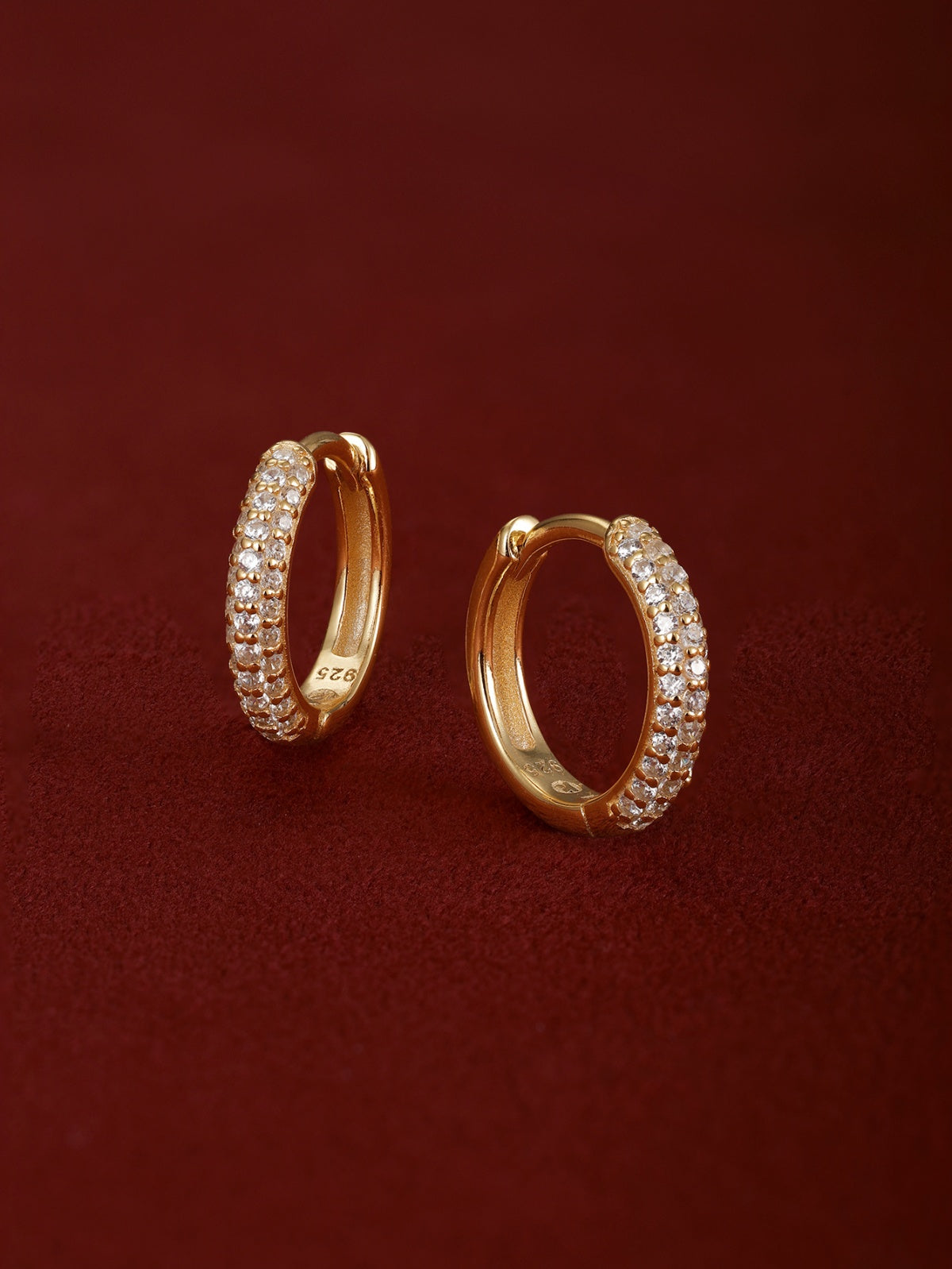 Matching pair of KOSINER Essentials gold-plated 925 sterling silver mini clicker hoops fully encrusted with double row pavé round crystals, inner band stamped 925, shot on soft burgundy suede fabric background