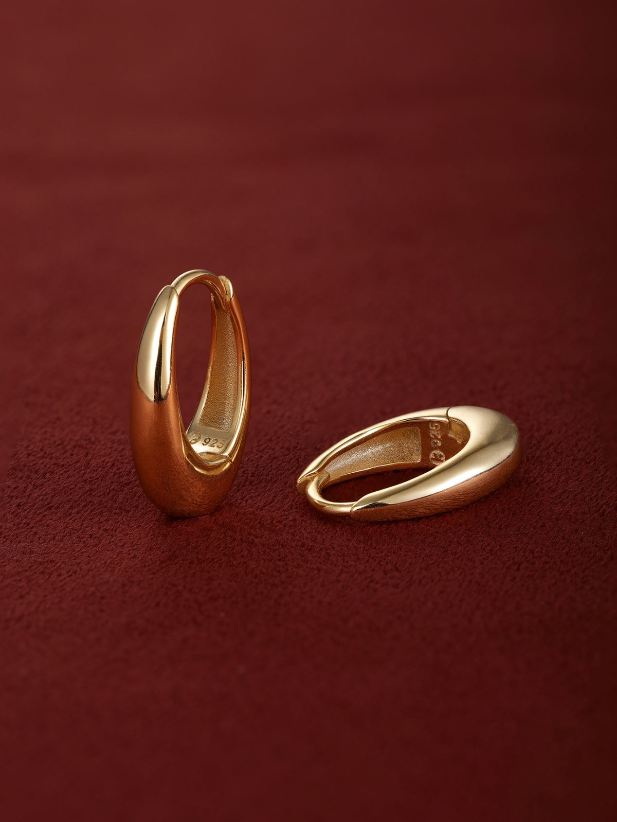 Matching pair of KOSINER Essentials gold-plated 925 sterling silver smooth oval drop clicker hoops, polished thick teardrop frame, inner band stamped 925, shot on soft burgundy suede fabric surface