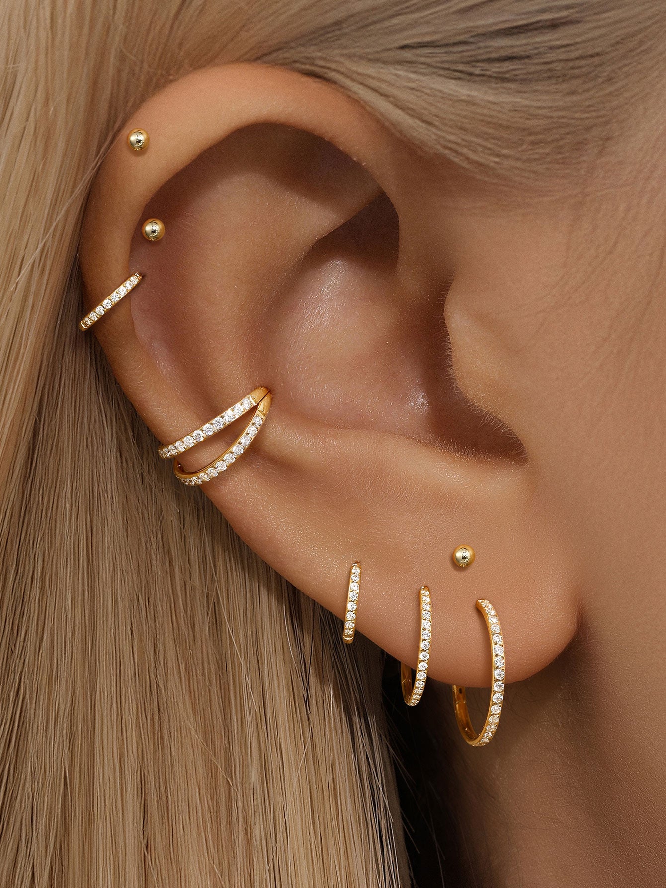 Model ear adorned with multiple gold titanium hoop earrings and cz studs, showcasing styling options.