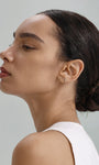 Elegant everyday styling with KOSINER Seaspritz tiny seahorse flat back stud on earlobe, model with neat low bun and plain neutral top, soft background showcasing petite wearable marine piercing jewelry