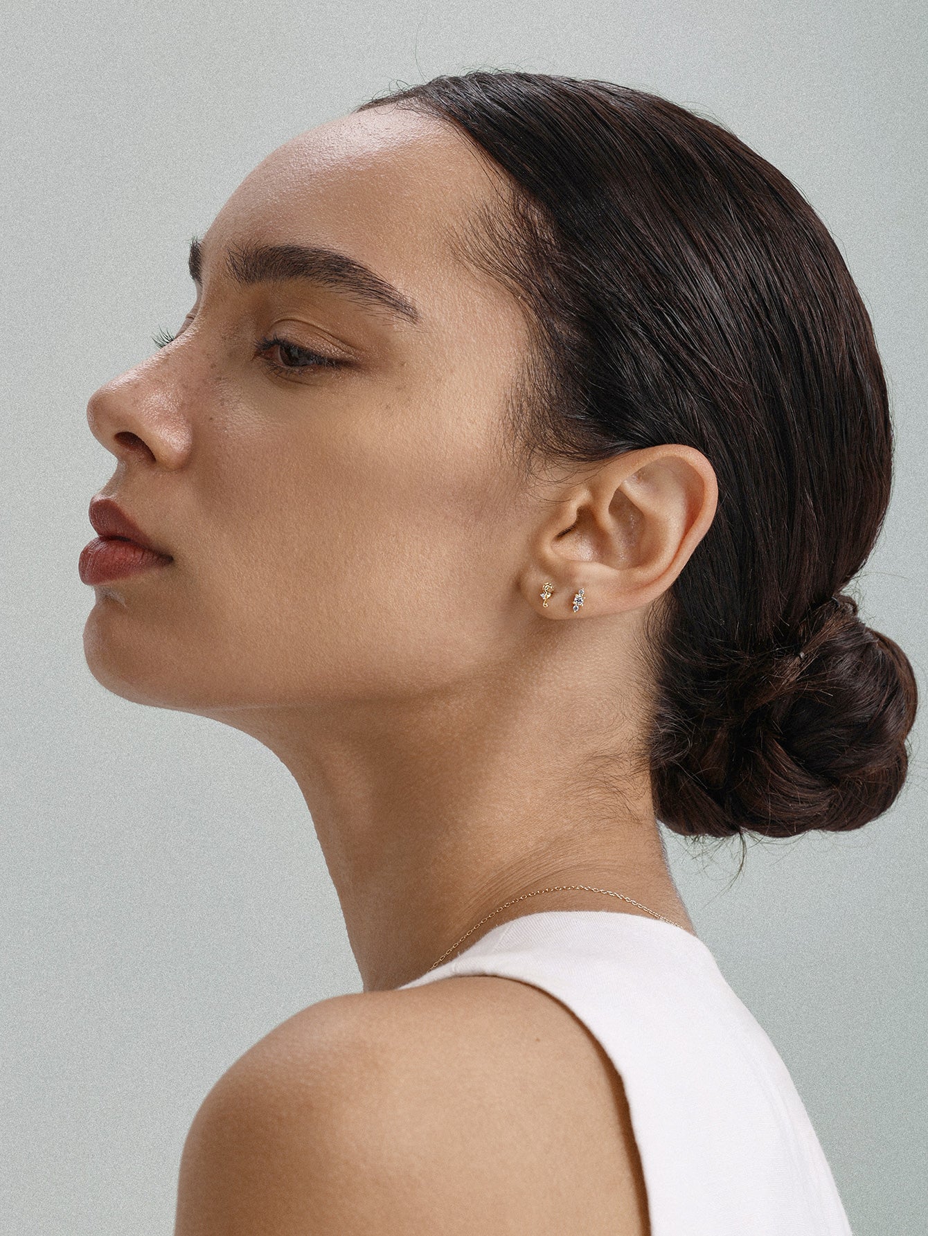Elegant everyday styling with KOSINER Seaspritz tiny seahorse flat back stud on earlobe, model with neat low bun and plain neutral top, soft background showcasing petite wearable marine piercing jewelry